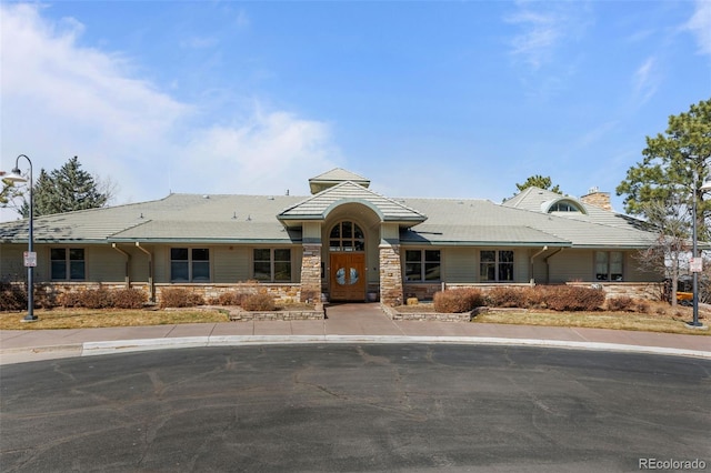 view of front of home featuring a tile roof, stone siding, and a chimney