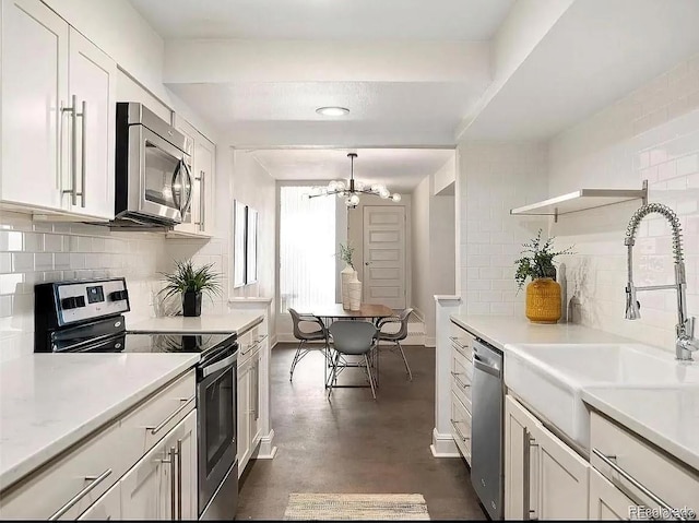 kitchen with sink, appliances with stainless steel finishes, backsplash, white cabinets, and a chandelier