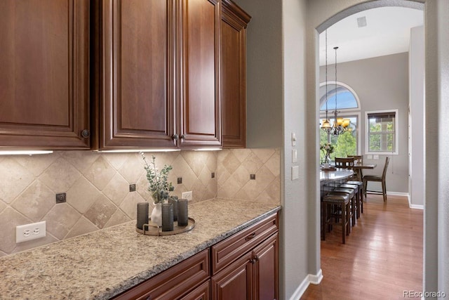 6299 Ellingwood Point Pl, Castle Rock, CO 80108 - kitchen featuring a chandelier, arched walkways, wood finished floors, and decorative backsplash