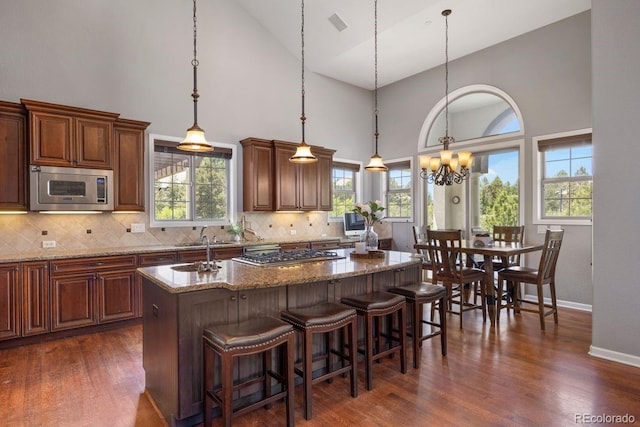 6299 Ellingwood Point Pl, Castle Rock, CO 80108 - kitchen with stainless steel appliances, a center island with sink, high vaulted ceiling, dark wood-style flooring, and a chandelier