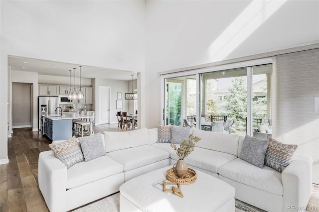 living room with an inviting chandelier, dark wood finished floors, a towering ceiling, and baseboards