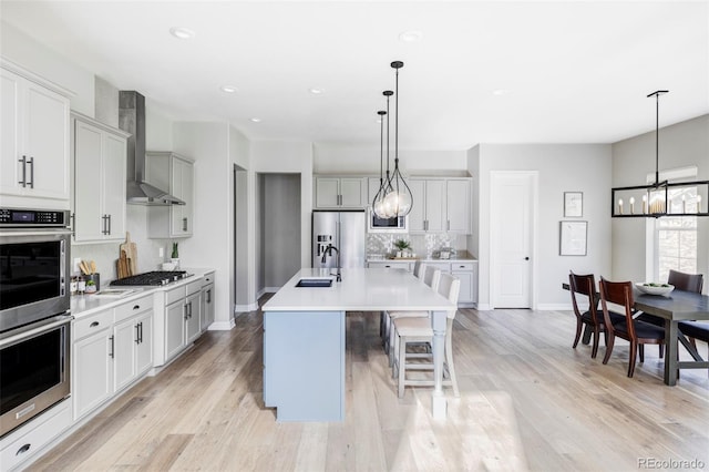 kitchen featuring appliances with stainless steel finishes, tasteful backsplash, a sink, an inviting chandelier, and wall chimney exhaust hood