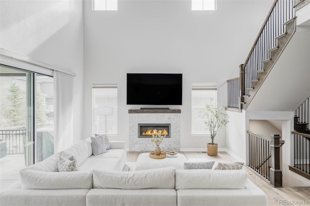 living area with a tile fireplace, wood finished floors, baseboards, a high ceiling, and stairs