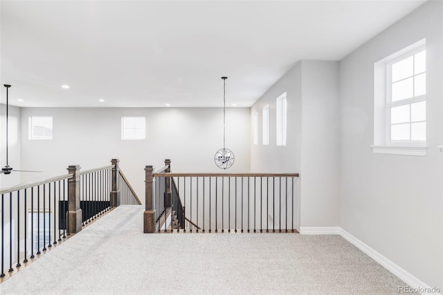 hallway with carpet floors, baseboards, a healthy amount of sunlight, and an upstairs landing
