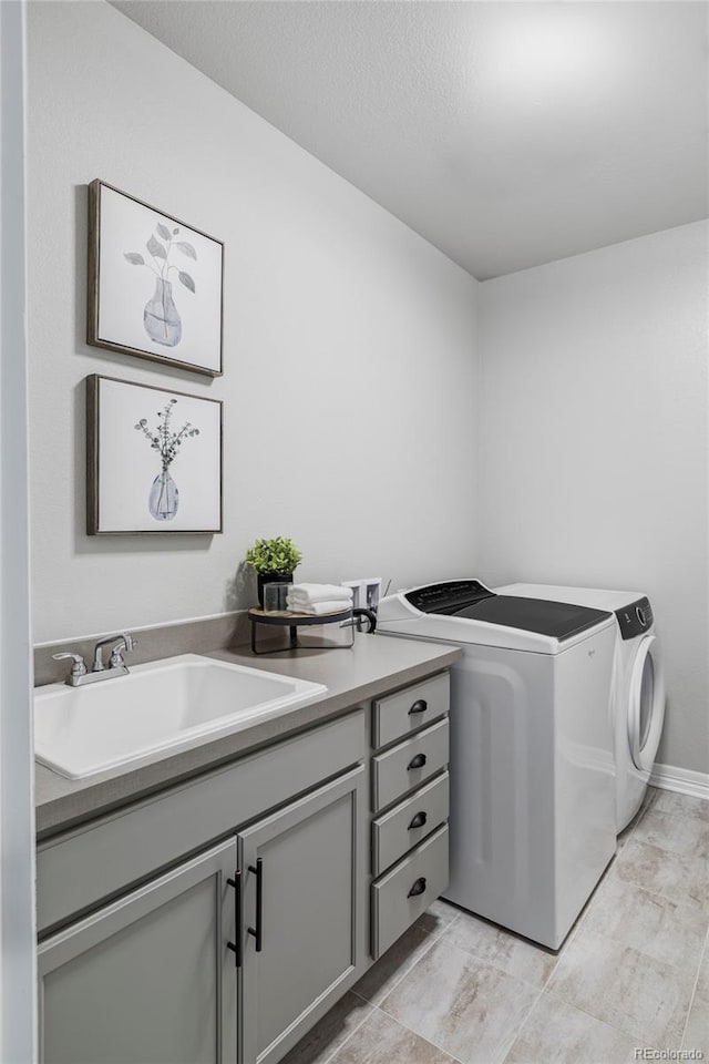 clothes washing area featuring cabinet space, washing machine and dryer, and a sink