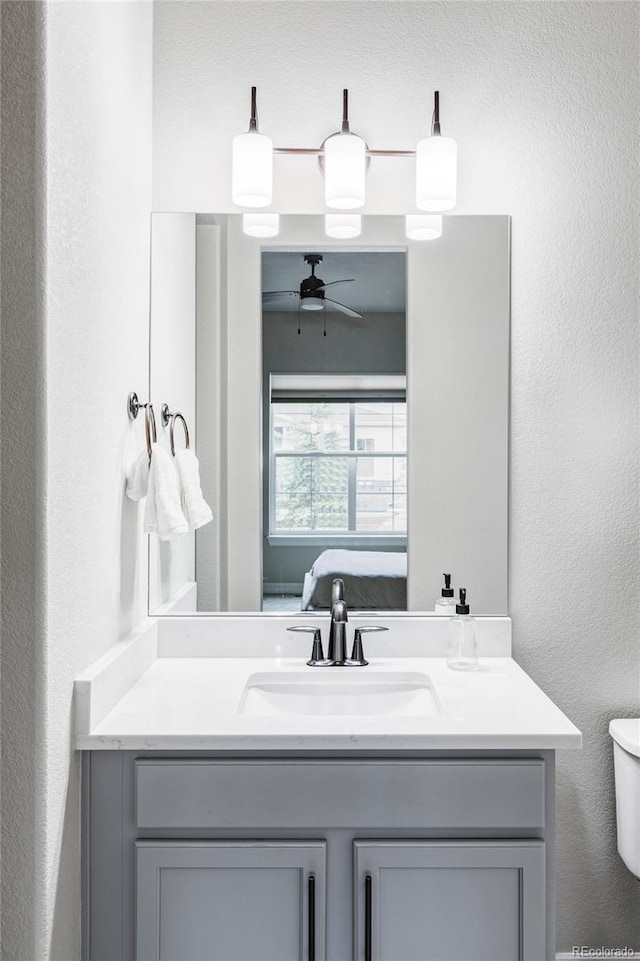 bathroom featuring vanity, a textured wall, ceiling fan, and toilet