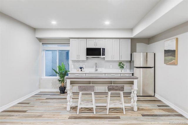 kitchen with a sink, appliances with stainless steel finishes, baseboards, and light wood-style floors