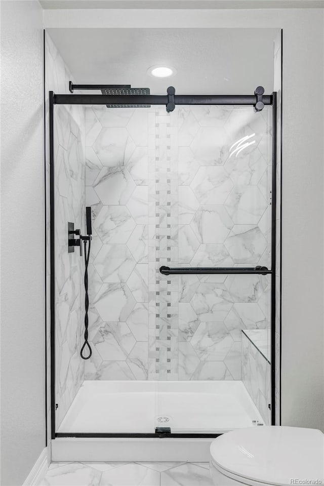 bathroom featuring marble finish floor, a stall shower, and toilet