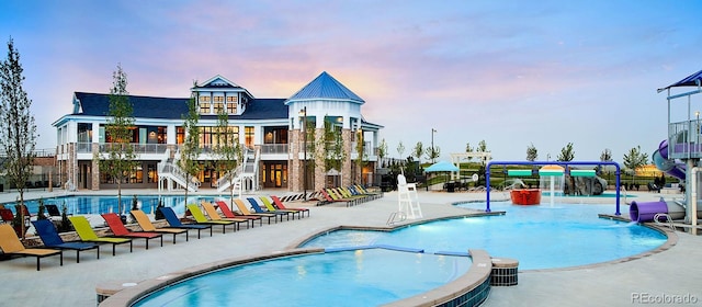 community pool with a water slide, stairs, and a patio