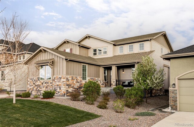 craftsman inspired home with a shingled roof, a front lawn, stone siding, board and batten siding, and covered porch