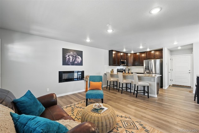 living area featuring baseboards, light wood finished floors, a glass covered fireplace, and recessed lighting