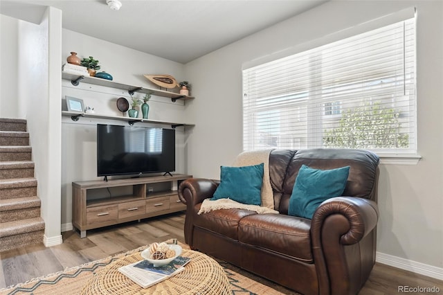 living area with baseboards, stairway, and light wood finished floors
