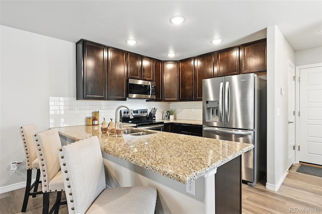 kitchen featuring light wood-style floors, dark brown cabinetry, light stone counters, stainless steel appliances, and baseboards