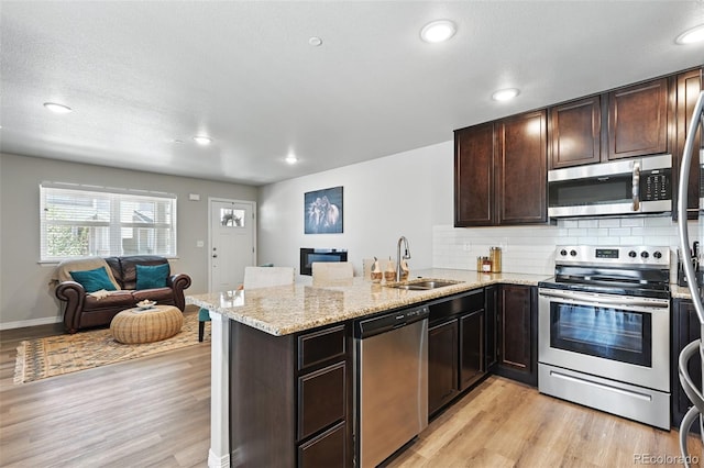 kitchen featuring light wood-style floors, a peninsula, appliances with stainless steel finishes, a sink, and open floor plan