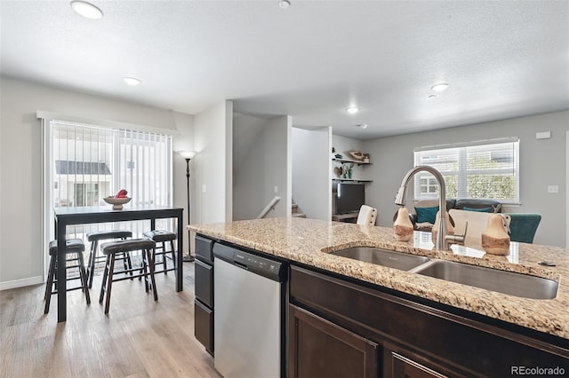 kitchen with light wood-style floors, dark brown cabinetry, light stone counters, dishwasher, and a sink