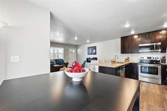 kitchen with dark brown cabinetry, tasteful backsplash, a sink, stainless steel appliances, and open floor plan