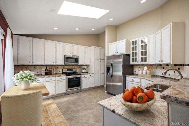 6480 Moss Cir, Arvada, CO 80007 - kitchen featuring appliances with stainless steel finishes, decorative backsplash, a skylight, light stone counters, and lofted ceiling