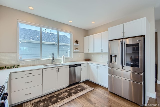 kitchen with stainless steel appliances, white cabinetry, a sink, and wood finished floors