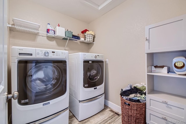 laundry room with light wood-style flooring, separate washer and dryer, visible vents, baseboards, and cabinet space