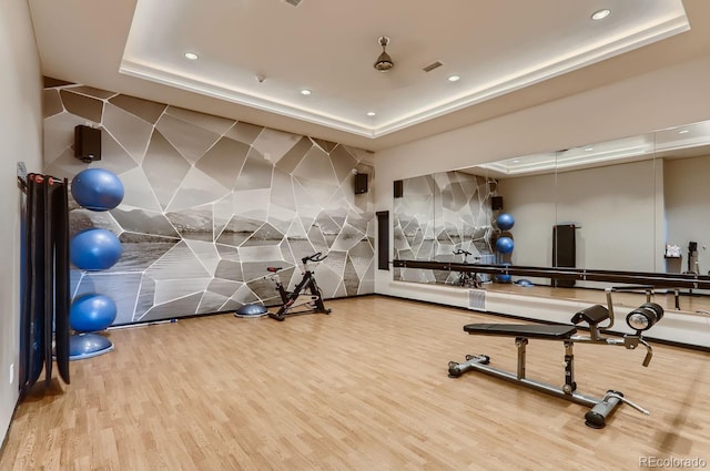 workout area with a tray ceiling, visible vents, recessed lighting, and wood finished floors