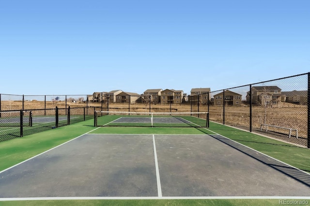 view of tennis court with fence and a residential view