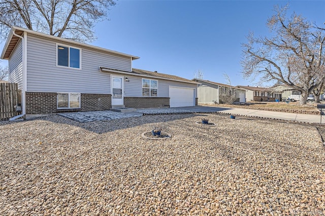 tri-level home with brick siding, driveway, an attached garage, and fence