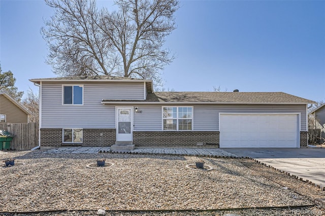 split level home featuring a garage, brick siding, driveway, and fence