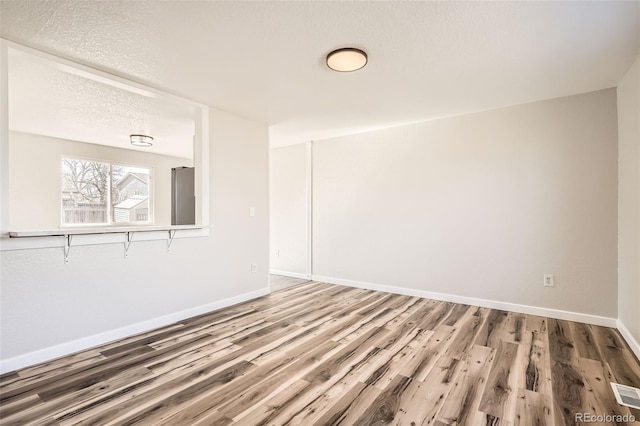 unfurnished room with a textured ceiling, baseboards, and wood finished floors