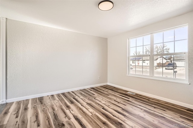 spare room featuring light wood-style floors, visible vents, a textured ceiling, and baseboards