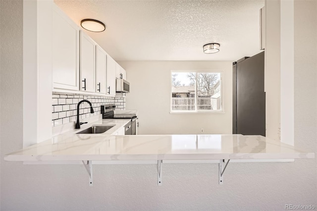 kitchen featuring stainless steel appliances, decorative backsplash, a sink, a textured ceiling, and light stone countertops