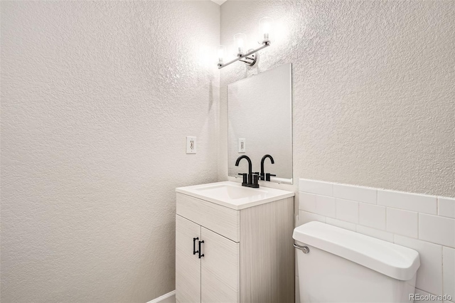 bathroom with toilet, vanity, tile walls, and a textured wall