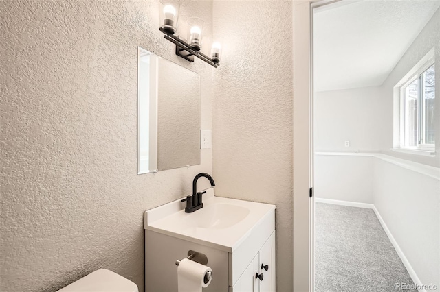 bathroom with a textured wall, vanity, and toilet