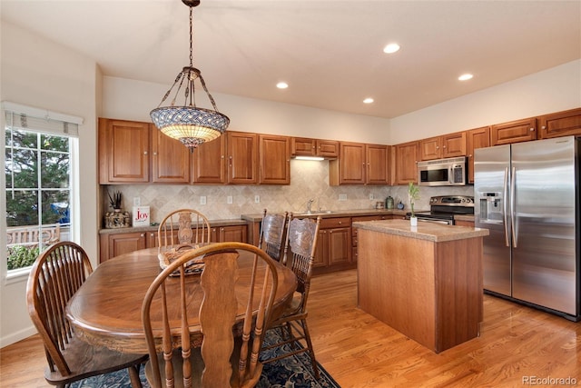 kitchen featuring hanging light fixtures, light wood-type flooring, tasteful backsplash, a kitchen island, and stainless steel appliances