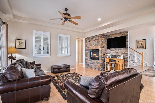 living room featuring stairway, a tray ceiling, a fireplace, and light wood-style flooring