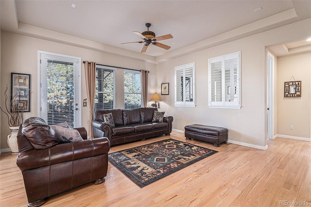 living area featuring light wood-style floors, baseboards, a tray ceiling, and a ceiling fan