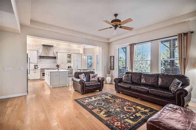 living room featuring light wood-style floors, a tray ceiling, ceiling fan, and baseboards