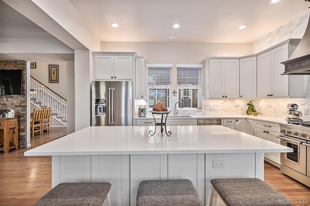 kitchen with light wood finished floors, premium range hood, high quality appliances, and backsplash