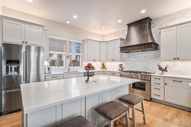 kitchen featuring premium appliances, light wood-style flooring, a breakfast bar area, custom exhaust hood, and a sink