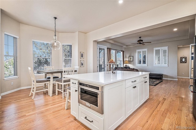 kitchen with a kitchen island, white cabinetry, light wood-type flooring, built in microwave, and plenty of natural light