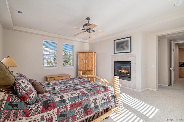 carpeted bedroom featuring ceiling fan, baseboards, a raised ceiling, and a tiled fireplace