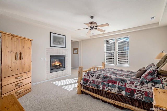 carpeted bedroom featuring a raised ceiling, visible vents, ceiling fan, and a tiled fireplace