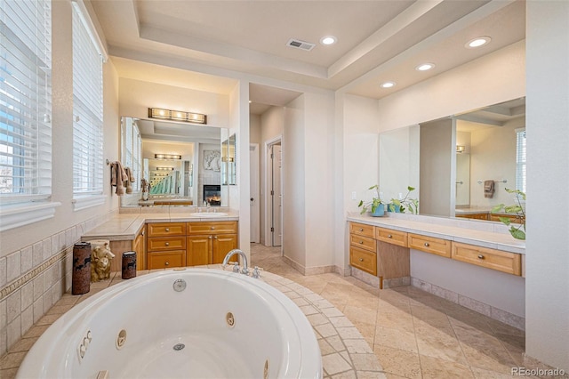 full bathroom with a tray ceiling, recessed lighting, visible vents, vanity, and a jetted tub