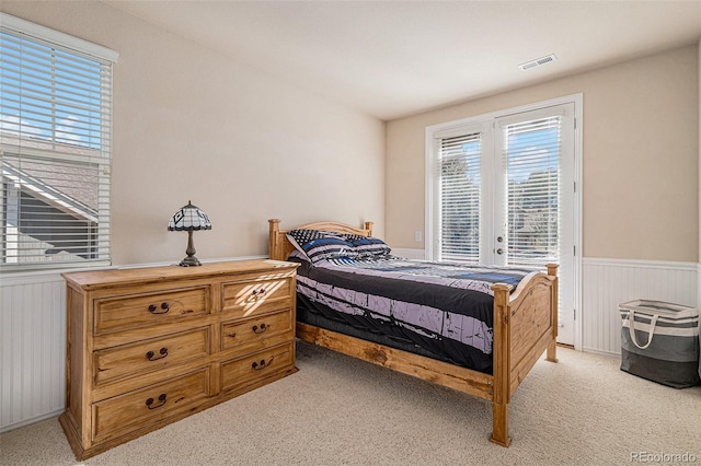 bedroom featuring light carpet, access to exterior, visible vents, and wainscoting