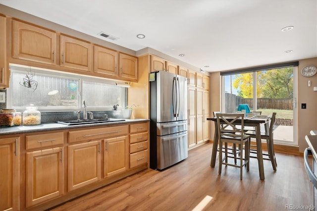 kitchen featuring light brown cabinetry, backsplash, sink, light hardwood / wood-style flooring, and stainless steel refrigerator