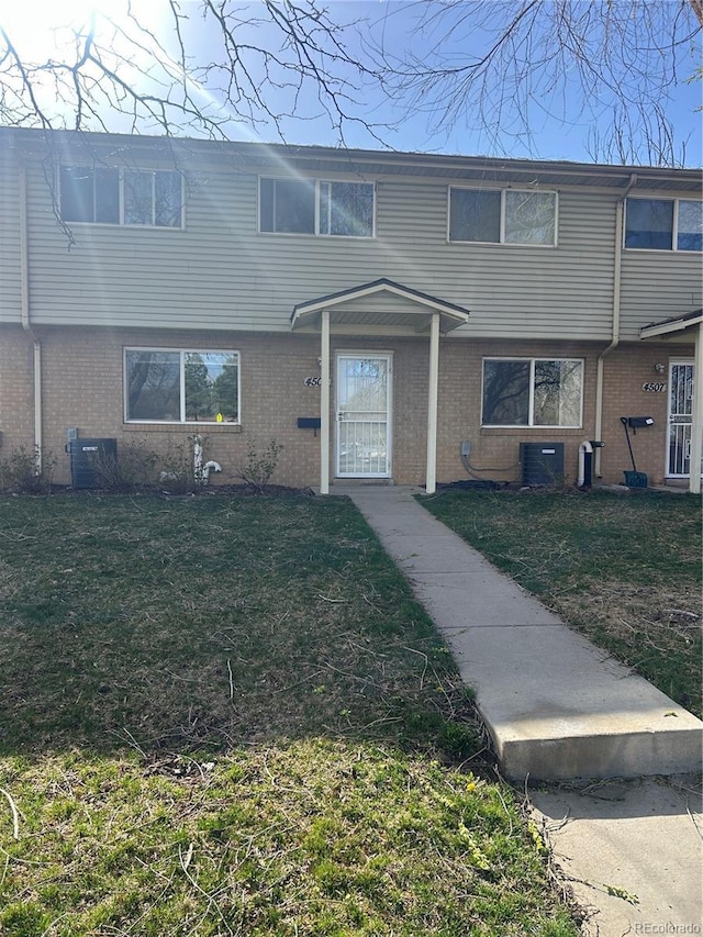 view of front facade with brick siding, central AC unit, and a front lawn