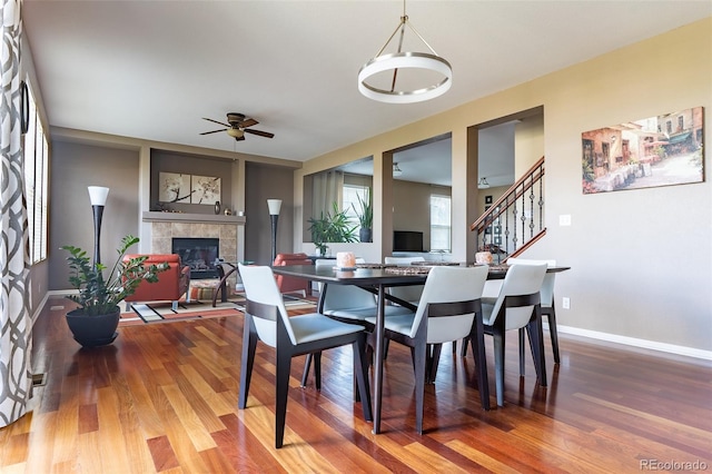 dining space featuring a tiled fireplace, ceiling fan with notable chandelier, and hardwood / wood-style floors