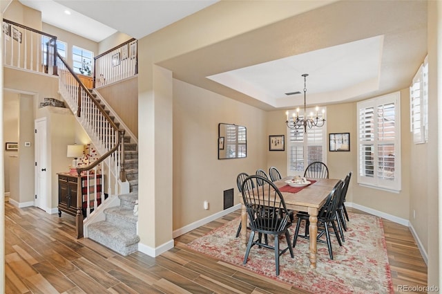 dining area with hardwood / wood-style flooring, a raised ceiling, and a notable chandelier