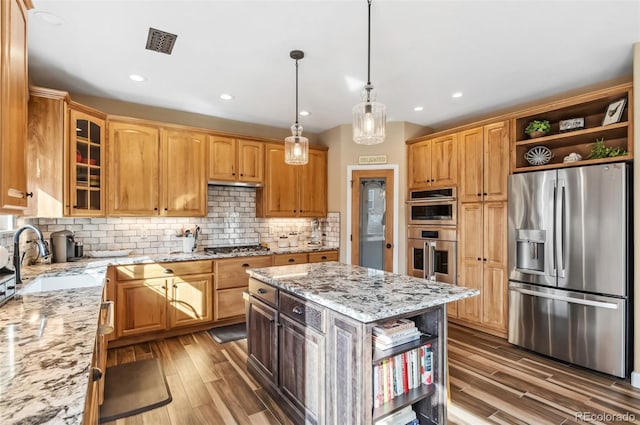 kitchen with sink, stainless steel appliances, light stone countertops, a kitchen island, and decorative backsplash