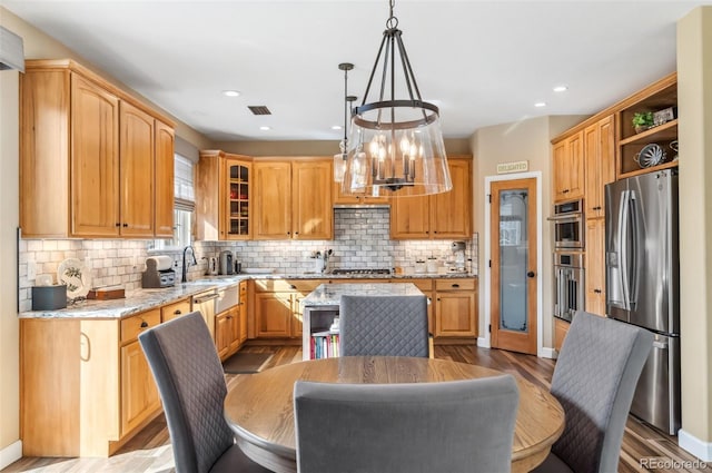 kitchen with stainless steel appliances, a center island, light stone counters, light hardwood / wood-style floors, and decorative light fixtures