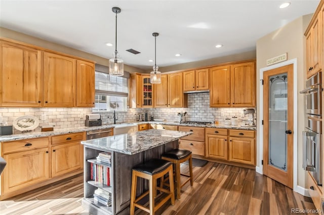 kitchen featuring light stone counters, a kitchen island, pendant lighting, hardwood / wood-style floors, and backsplash